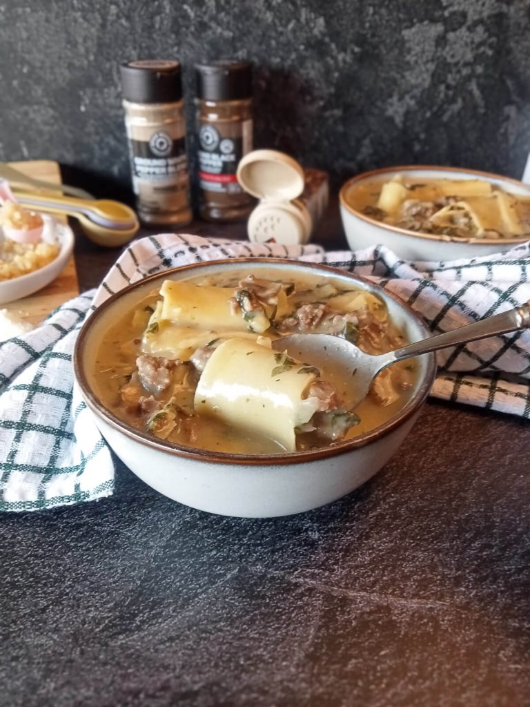 Creamy Alfredo lasagna soup in a bowl on a black background with other cooking utensils.