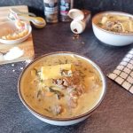 Creamy Alfredo lasagna soup in a bowl on a black background with other cooking utensils.