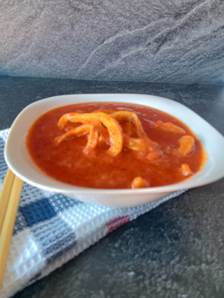 Baby squid soup in a white bowl with a tablecloth underneath on a black background