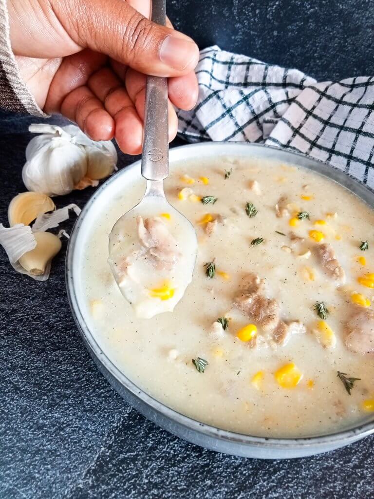 a hand scooping chomarro corn soup from a grey bowl with a silver spoon.