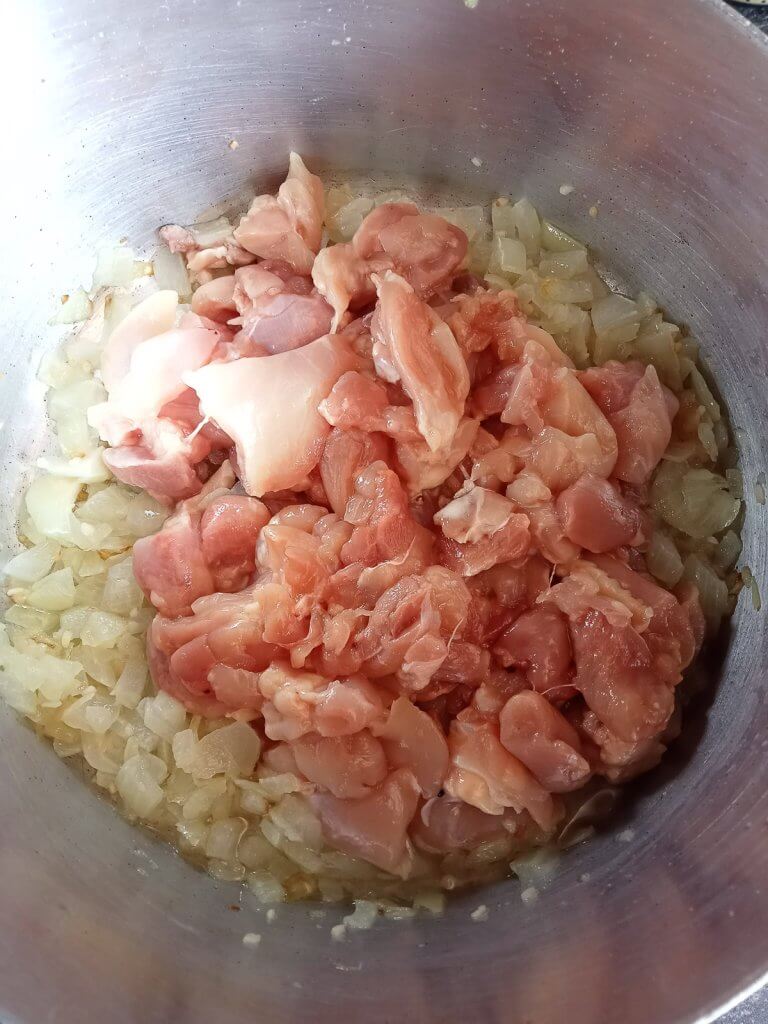 raw chicken added to a pot to be cooked with sauteed onions.