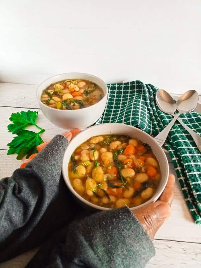 two human hands holding a bowl of dilly bean stew.