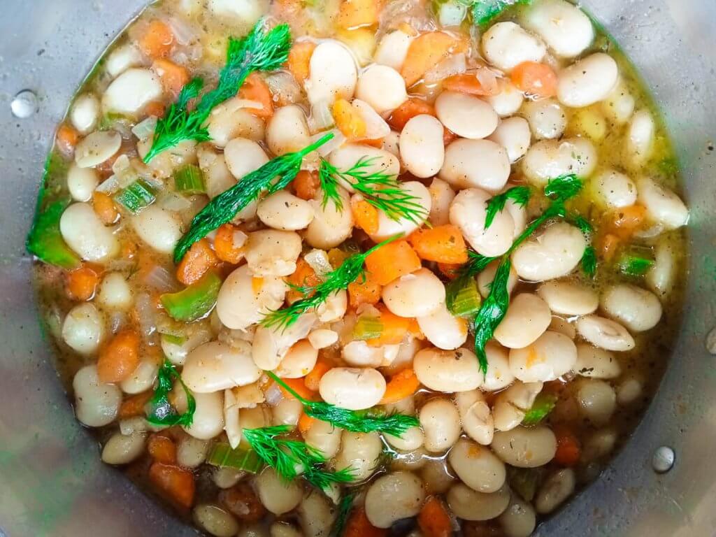 a pot full of beans, carrots, dill, and broth.