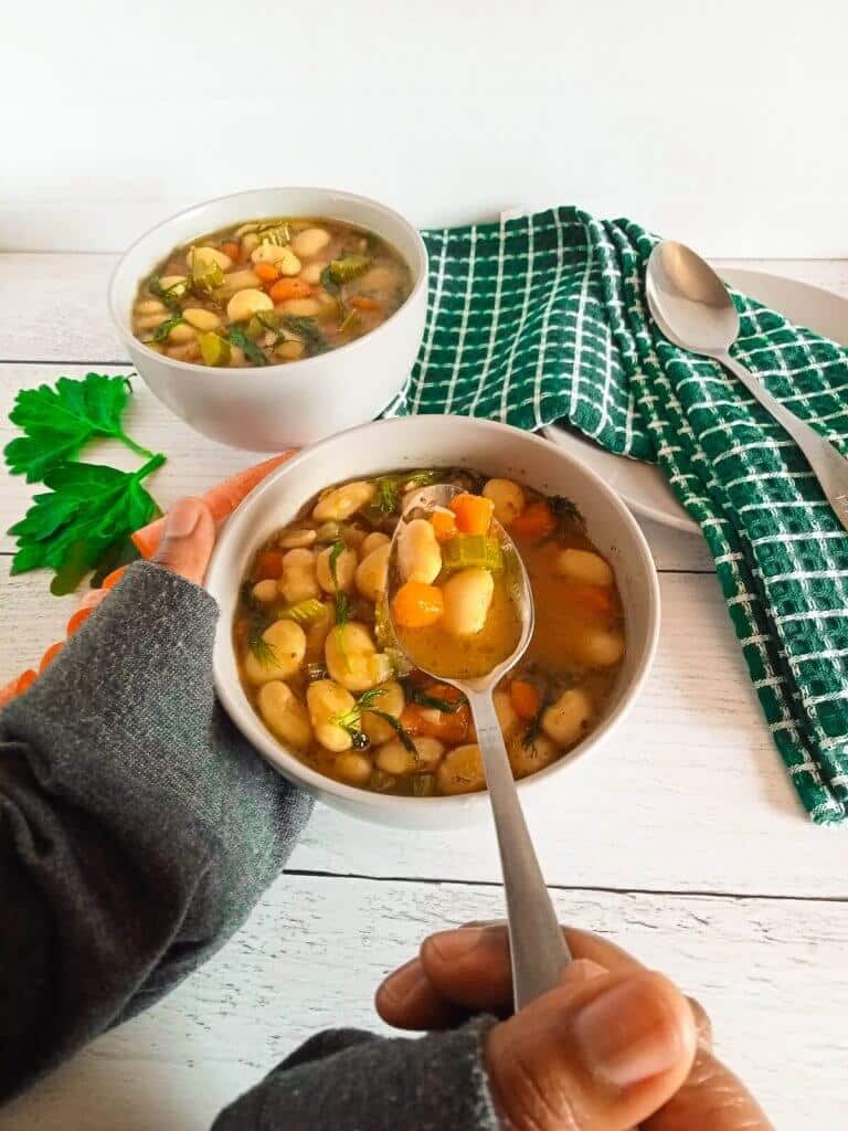 dilly bean soup scooped with a silver spoon from a bowl on a white background.