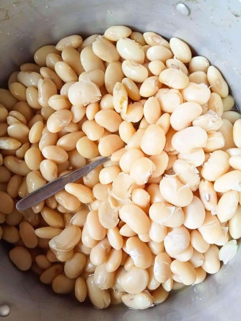 White beans in a pot with a silver metal spoon in them.