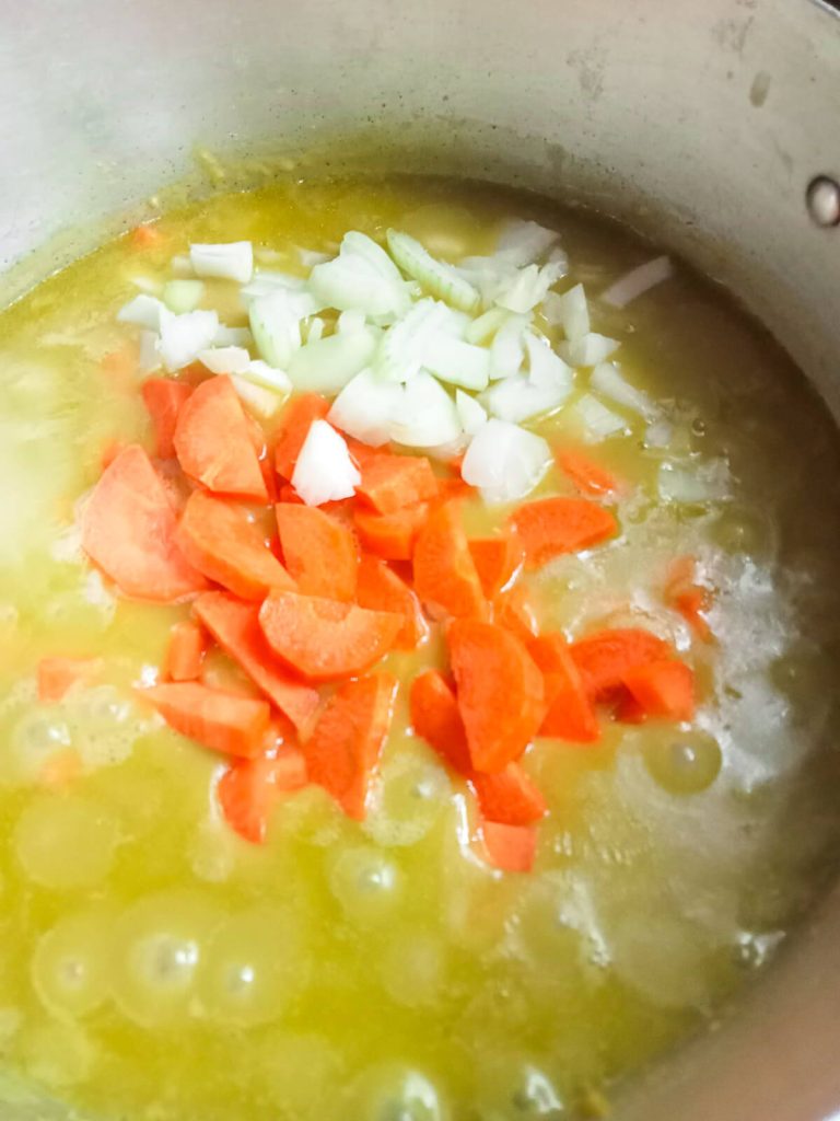 A process photo of a metal pot with onions, carrots, and green split peas and broth in it.