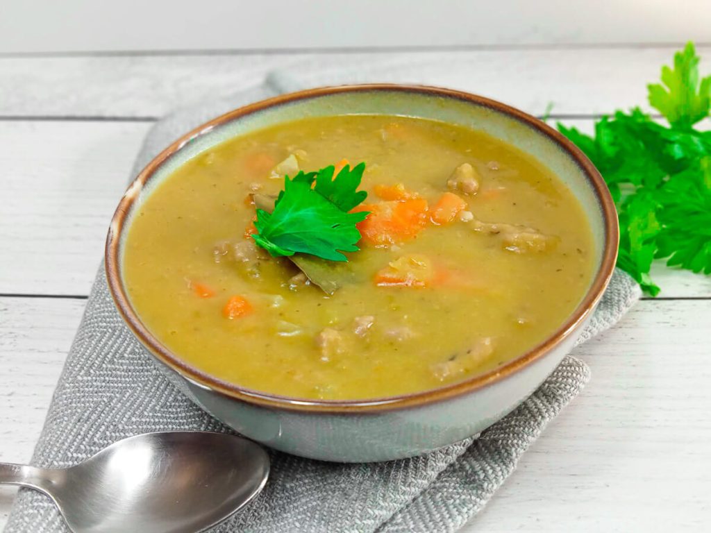 a close up image of a bowl full of green split Pea soup garnished with fresh leaves of herbs on a grey table cloth and withe background.