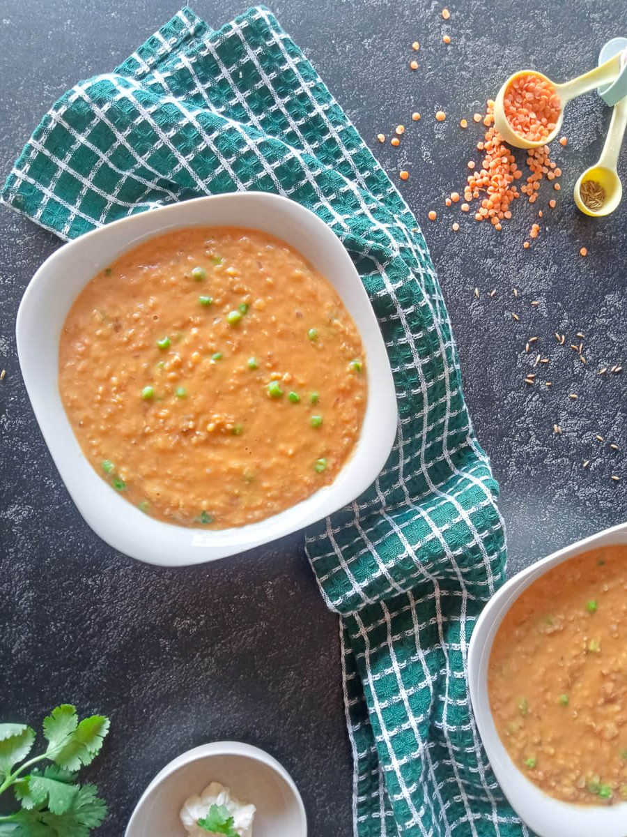 bone broth lentil soup in white bowls on a black background with a green tablecloth and few unused ingredients