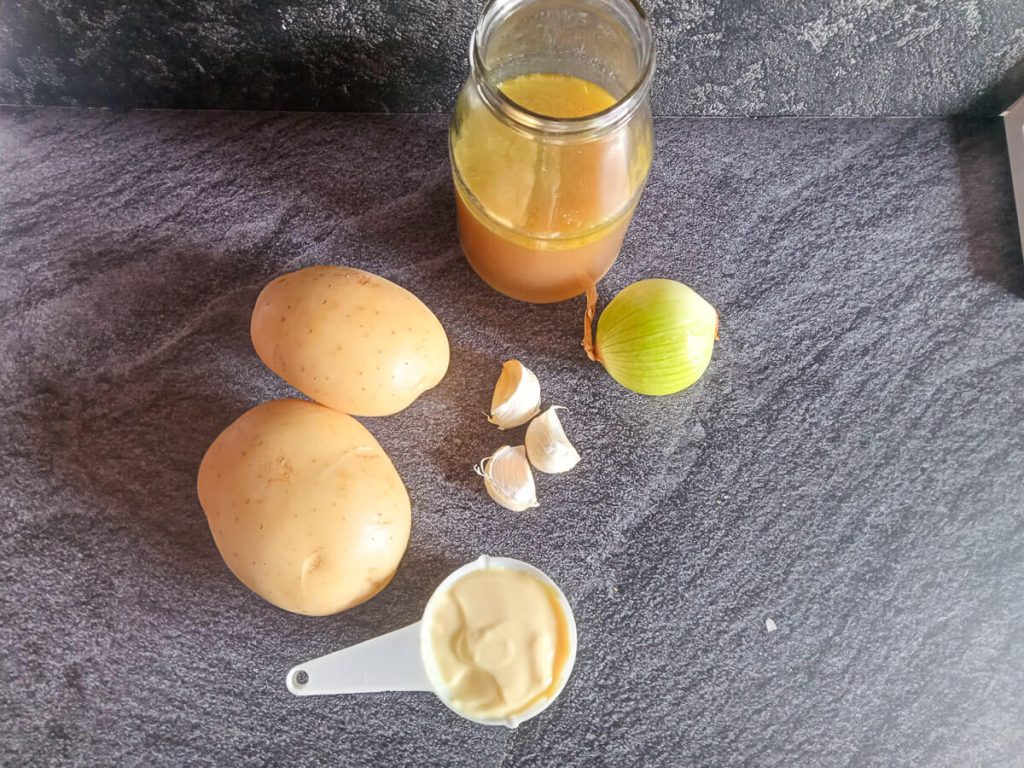 Ingredients photo with a bottle full of broth, a cup of mayonnaise, garlic, potatoes and onion.