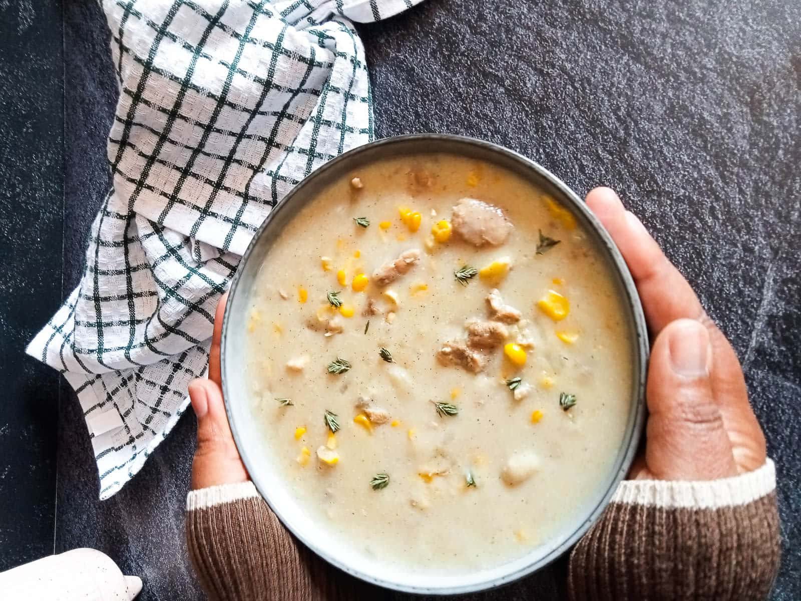 a bowl of chomarro corn soup in a lady's hands with a tablecloth near by.