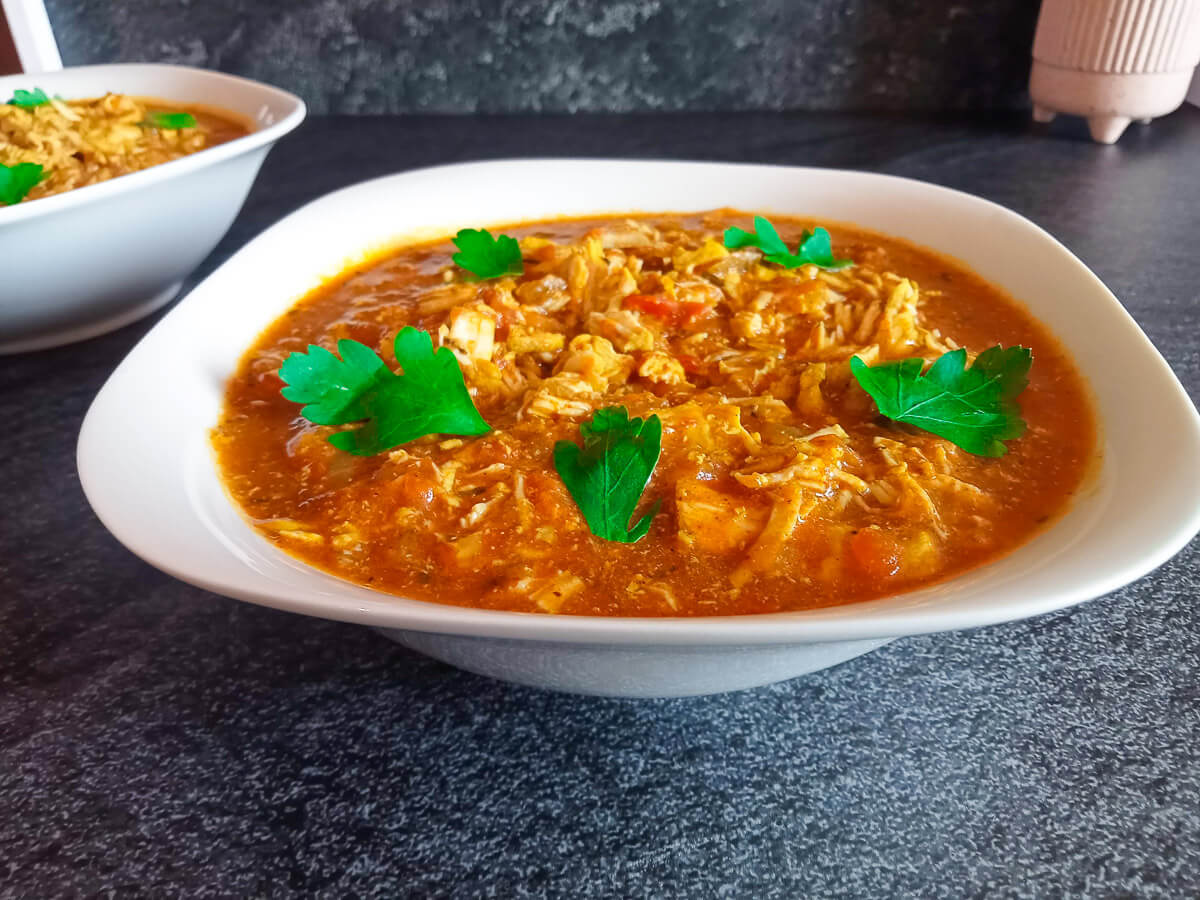 a white bowl of chicken tinga soup garnished with fresh herbs on a black background.