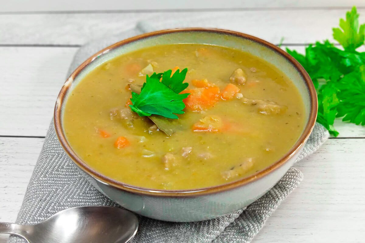 a close up image of a bowl full of green split Pea soup garnished with fresh leaves of herbs on a grey table cloth and withe background.