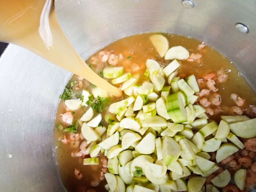 Stock poured into a pot with vegetables in it.