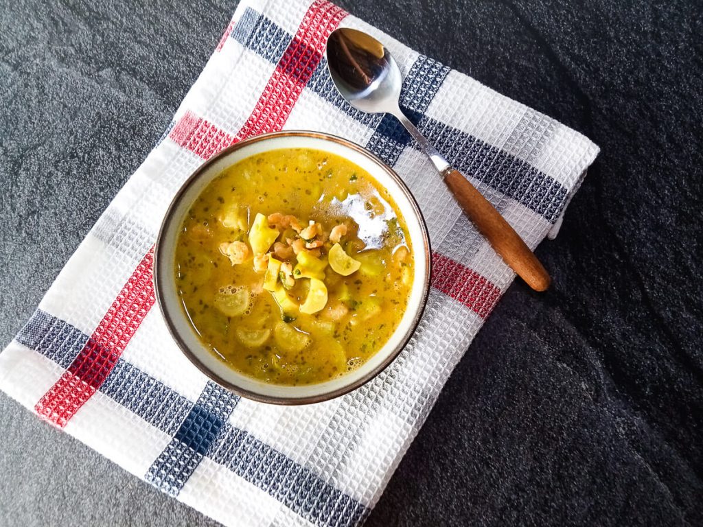 a bowl of Vietnamese Opo squash soup on top of a table cloth with a silver and wooden spoon next to it