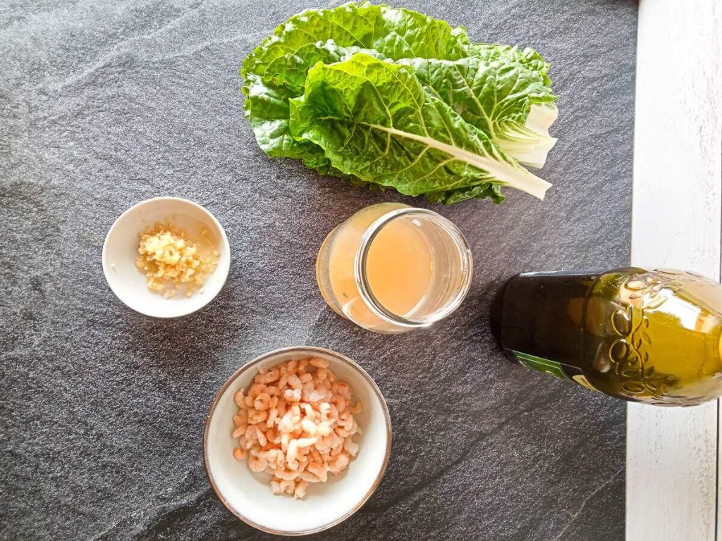 a photo of ingredients for a spinach soup. There is spinach, minced garlic, shrimp, chicken broth, and olive oil.