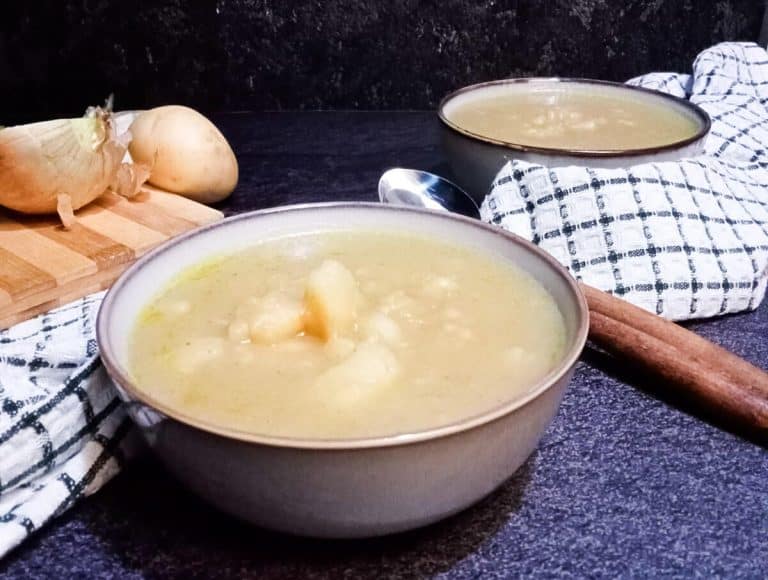 2 bowls of 3 ingredients potato soup with two spoons and a table cloth. There is left over ingredients on a chopping board in the background.