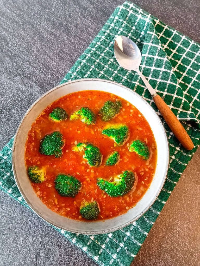 A bowl of broccoli tomato soup on a green and white table cloth with a spoon beside it with a black marble background.