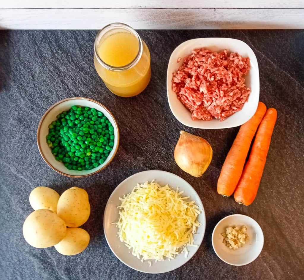 Ingredients photo shows a bowl of uncooked ground beef, carrots, onion, minced garlic, potatoes, green peas, beef broth, and shredded cheese.