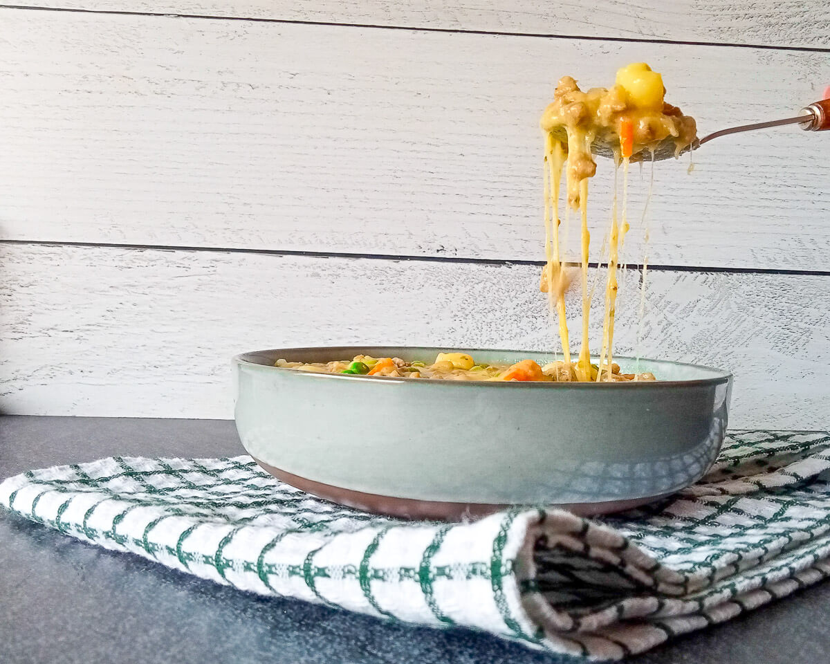 A bowl of potato hamburger soup on a white tablecloth shows a cheese pull effect on this recipe.