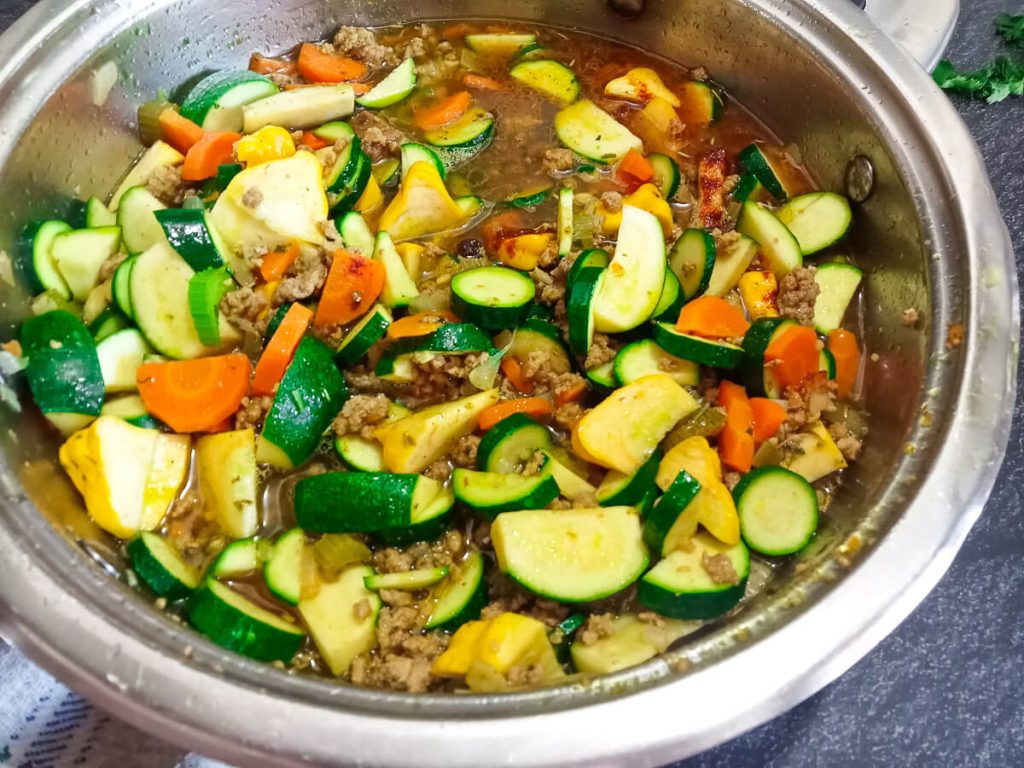 process photo- a variety of summer squash chopped and cooked with ground beef in a pot.