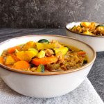 Close-up photo of Two bowls of rainbow soup on a grey tablecloth on a black background.
