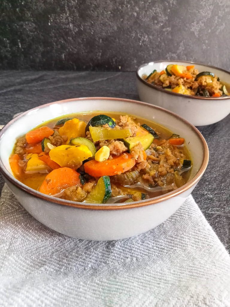 Two bowls of rainbow soup on a grey tablecloth on a black background.