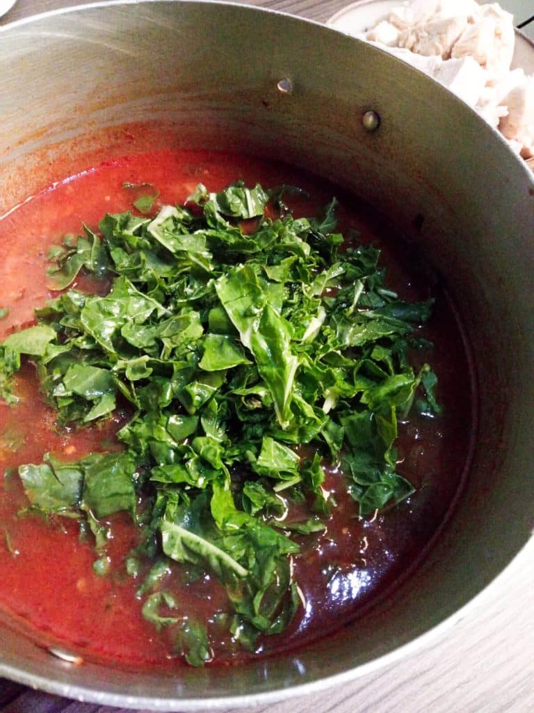 a pot with reddish soup and spinach.