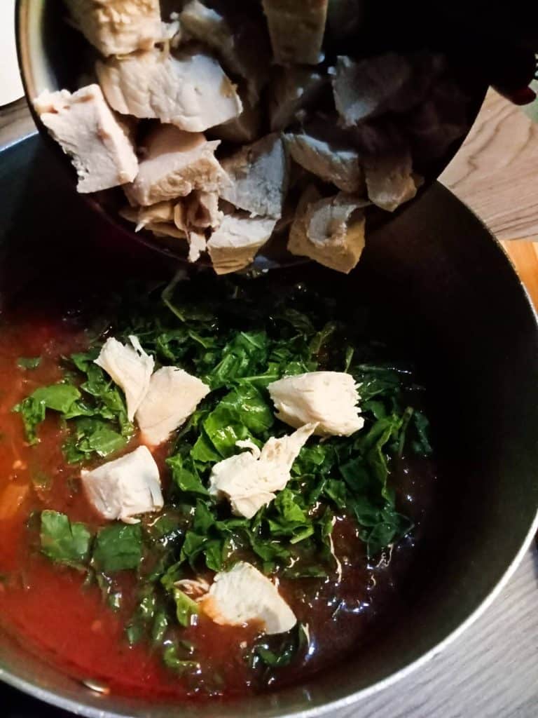 Adding pre cooked chicken cubes in a pot of Orzo spinach soup.