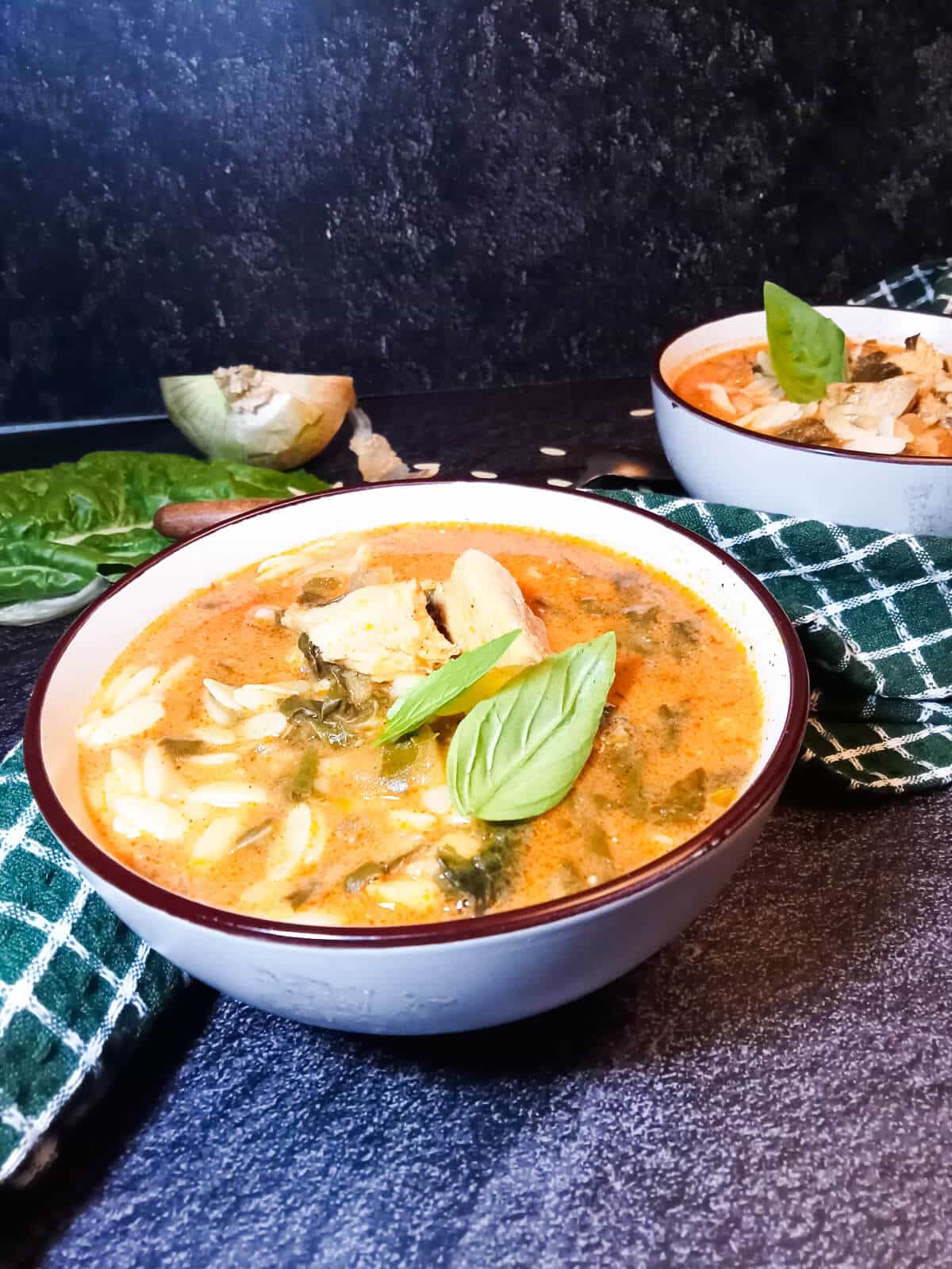 a bowl of rosa marina soup with chicken and spinach garnished with fresh herbs. There is a second bowl in the background and some left ingredients.