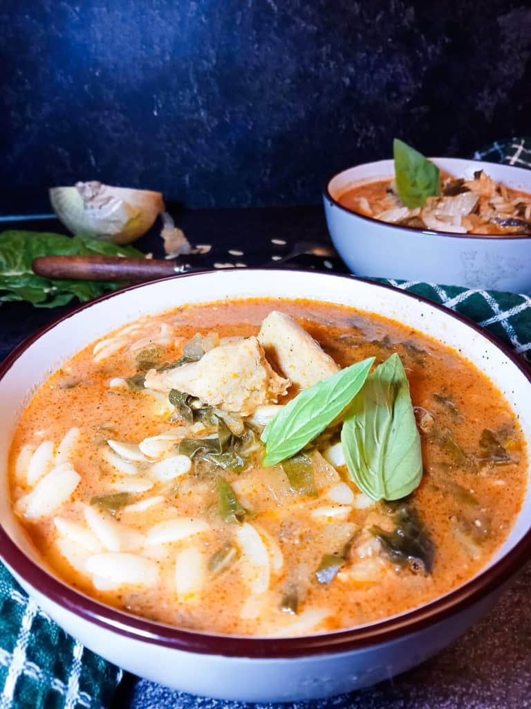 a bowl of rosa marina soup with chicken and spinach garnished with fresh herbs. There is a second bowl in the background and some left ingredients.