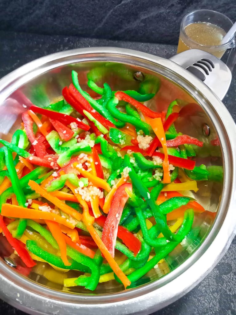 process photo of sliced peppers and onion with minced garlic in a pan.