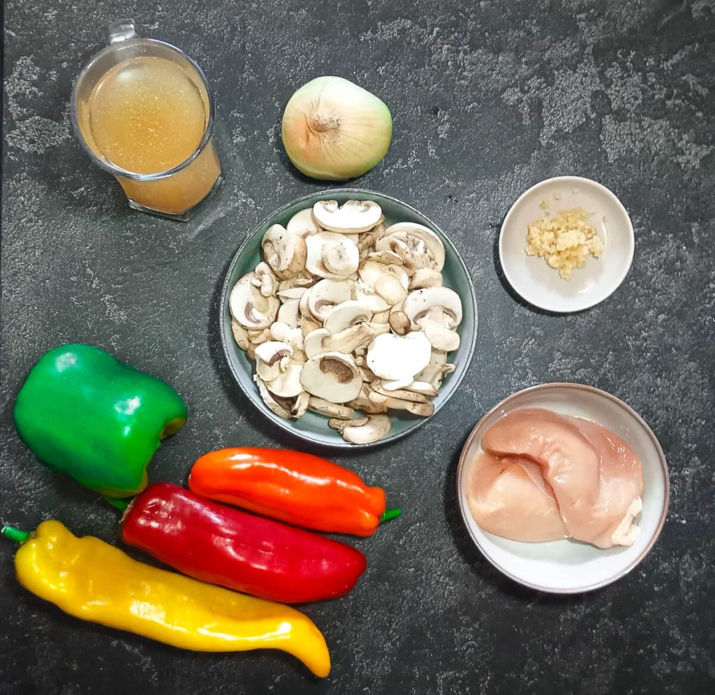 Ingredients images for stir fry soup recipe. There is chicken broth, onion, mushrooms, minced garlic in a bowl, chicken breasts in a bowl, red pepper, green pepper, yellow pepper, and orange pepper.