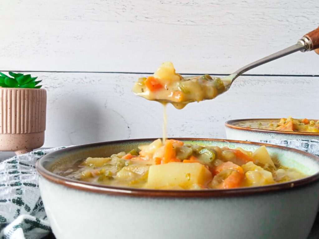 a close up shot of th Vomacka soup scooped in a spoon with another bowl in the background and some succulent plant.