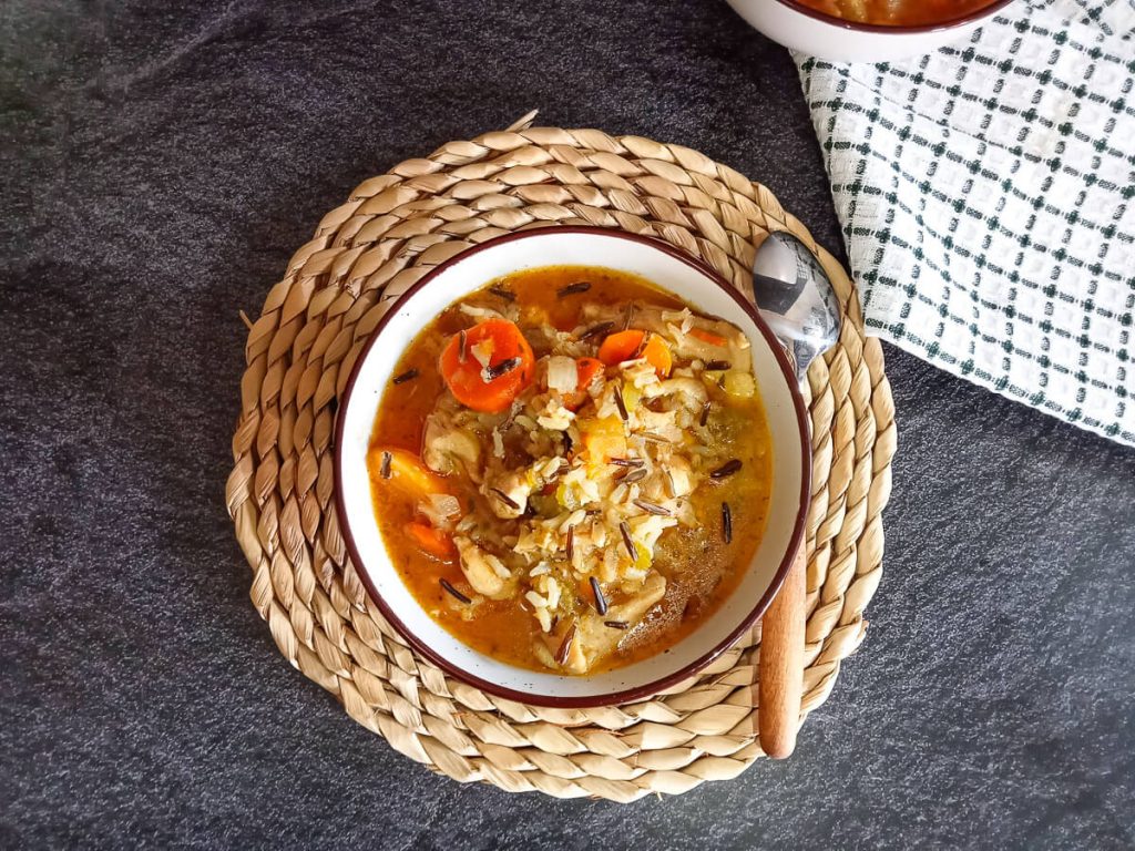 An overhead shot of a Cozy autumn wild rice soup bowl on a plate mat with a spoon beside it on a black background.