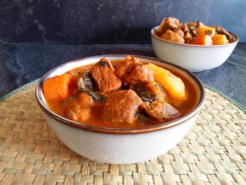 Two bowls of bouyon haitian soup on a plate mat with a black background.