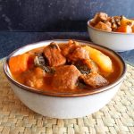 Two bowls of bouyon haitian soup on a plate mat with a black background.