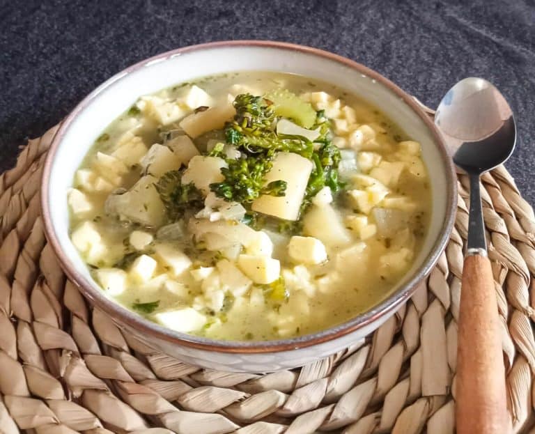 A bowl of broccoli feta soup on a plate mat with a spoon beside it on a black background.