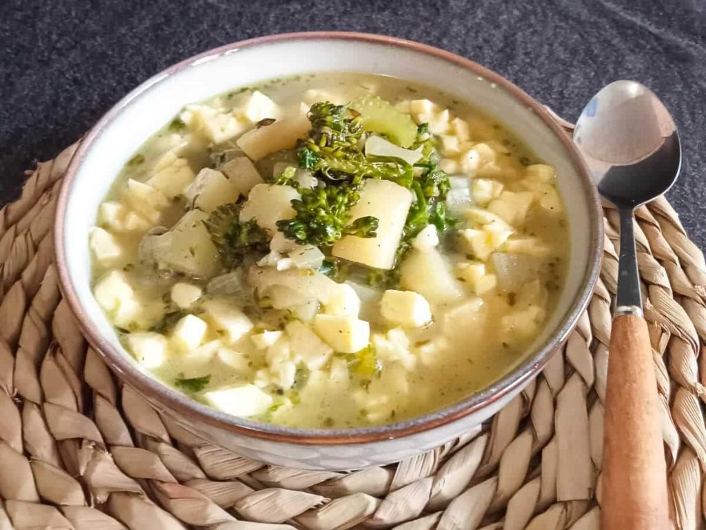 A bowl of broccoli feta soup on a plate mat with a spoon beside it on a black background.