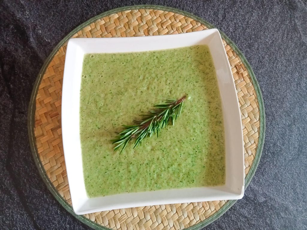 An overhead shot of a white bowl of broccoli and zucchini soup on a plate mat with a black background.