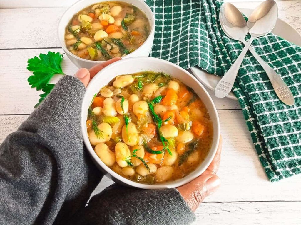 two human hands holding a bowl of white bean soup.