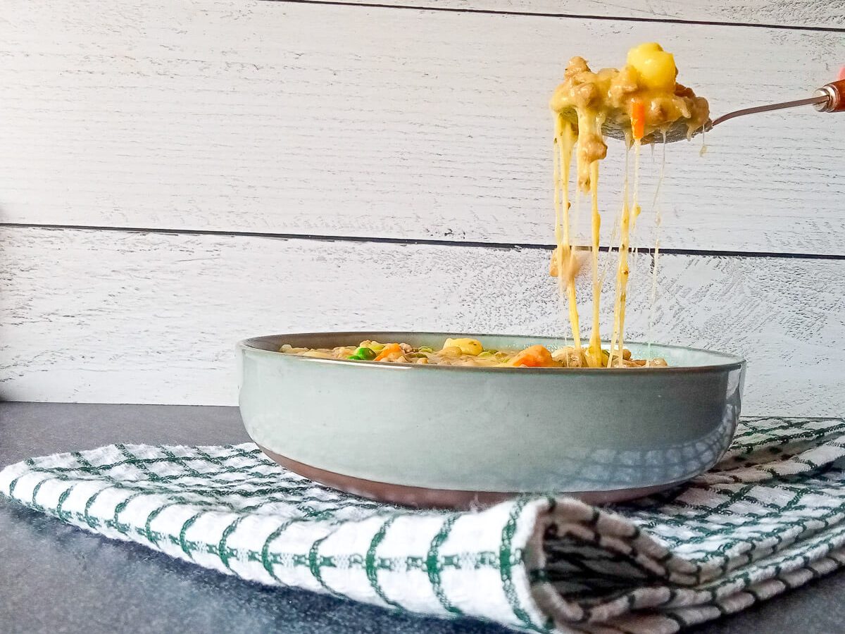 A bowl of potato hamburger soup on a white tablecloth shows a cheese pull effect on this recipe.