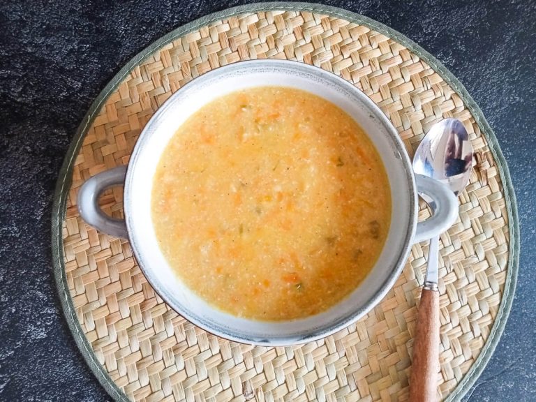 An overhead shot of a bowl of saltgrass potato soup on a plate mat with a spoon beside it.