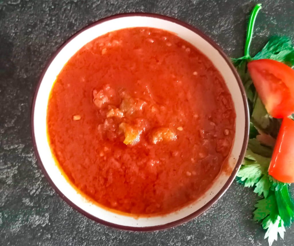 an overhead shot of a tomato celery soup with left over ingredients beside it on a black background.