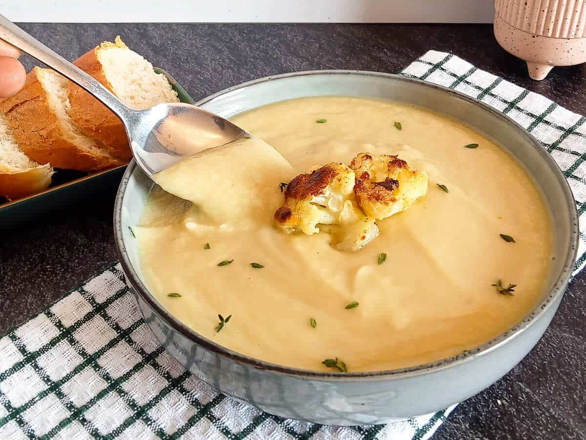 scooping cauliflower soup from a bowl with a spoon