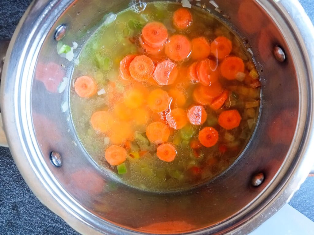 process photo: adding carrots and beef stock to the pot of soup