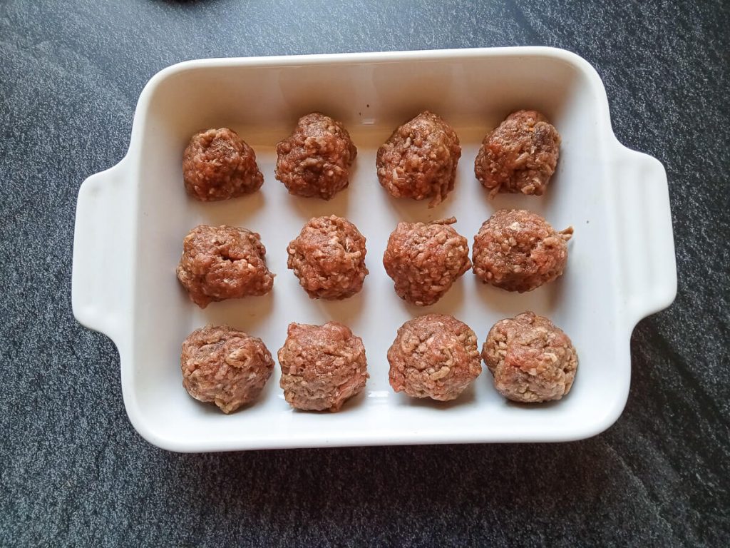 process photo: meatballs lined up in a baking dish to be baked in an oven.