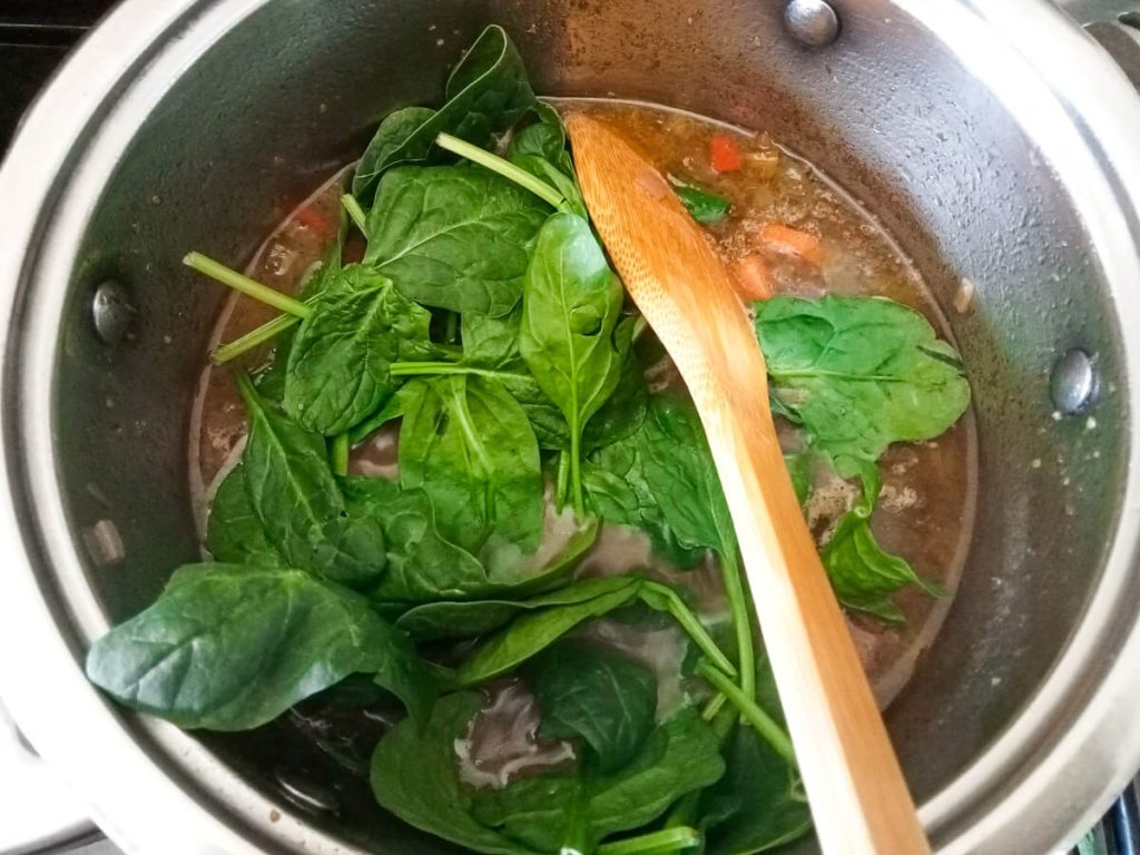 process image adding spinach to the pot of orzo pasta soup