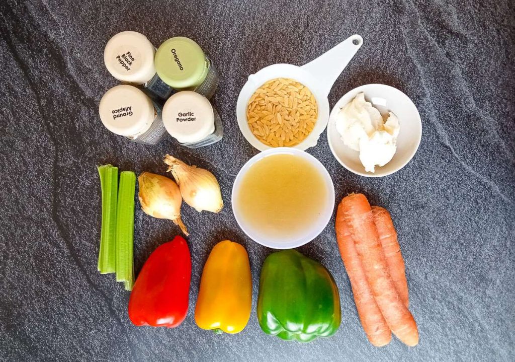 A photo of ingredients needed to cook a vegetable orzo soup recipe. On the image there's beef broth, bell peppers, carrots, celery, onion, orzo pasta, cream and seasoning