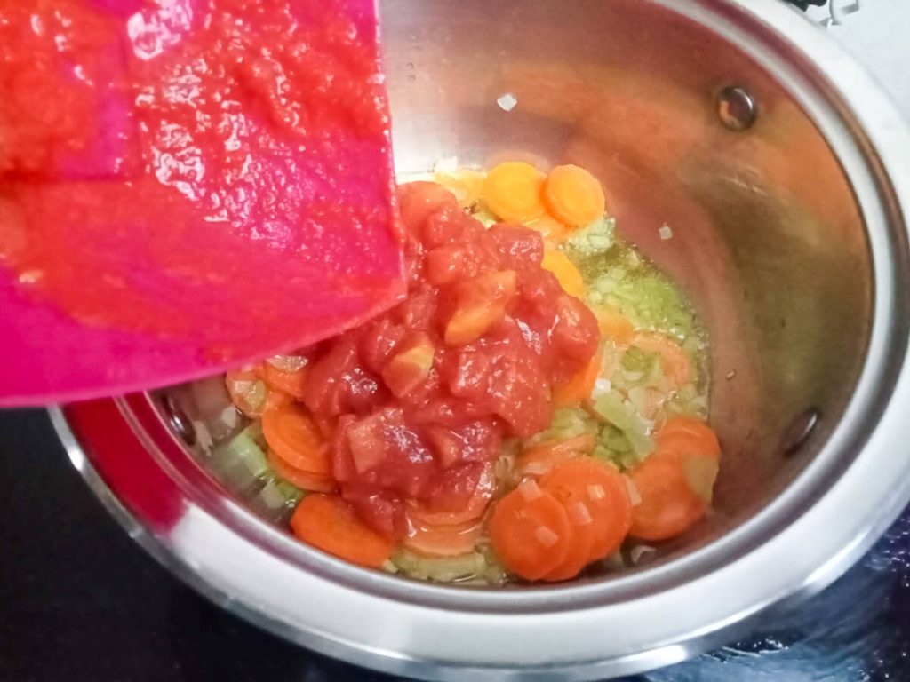 process image: Adding canned tomatoes into the pot of chicken noodle soup