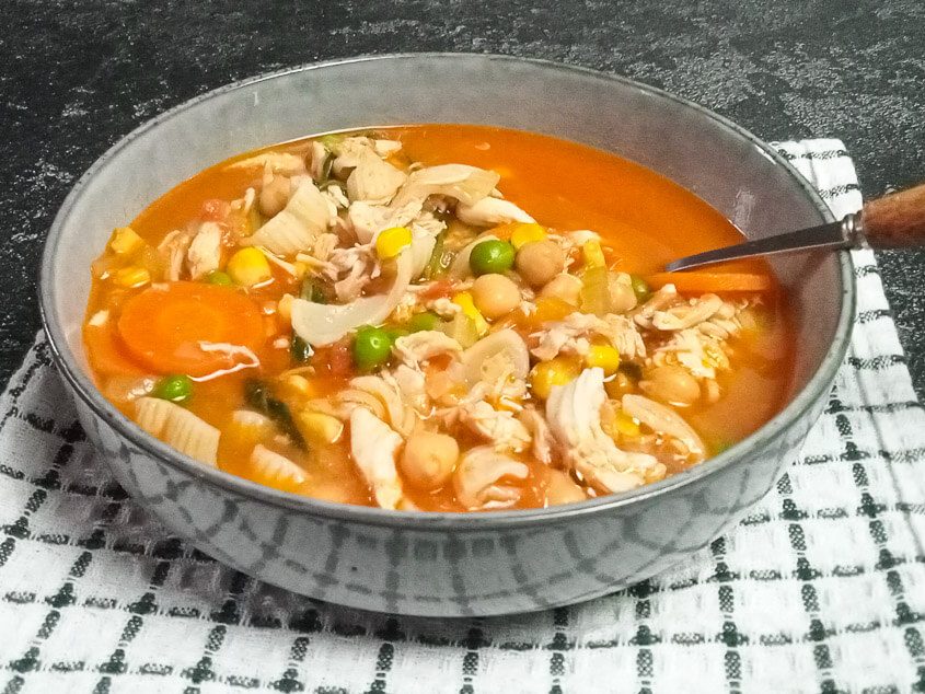 A shot of high-protein chicken noodles soup in a bowl on top of a white and green tablecloth with a black background